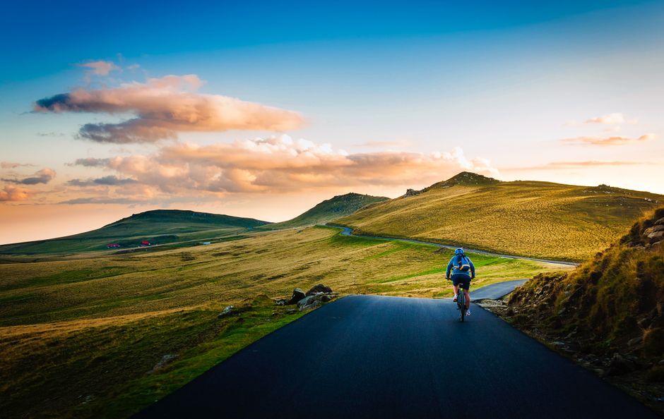 Cyclist biking on a scenic rural road with rolling hills at sunset.
